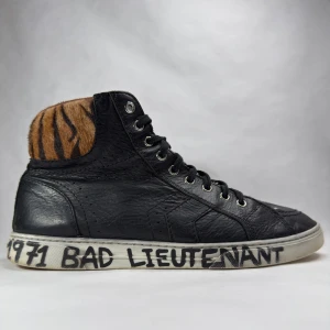 Saint Laurent svarta sneakers med tigerdetalj - Feta svarta high-top sneakers från Saint Laurent med tigerinspirerad pälsdetalj vid ankeln och handskriven text på sulan. Storlek 42 Nypris 7000kr 