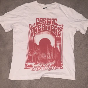 Vit t-shirt med röd tryck från Gina Tricot - Använt några gånger innan men slutade använda den efter en tag. Vit t-shirt från Gina Tricot med rött retroinspirerat tryck på framsidan där det står 'Cosmic Dreamers Soul Search'. Klassisk rund halsringning och korta ärmar. Perfekt för en avslappnad och cool stil.