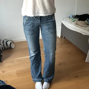 Blå bootcut jeans med fickdetaljer - Säljer ett par klassiska blå jeans med bootcut passform och snygga fickdetaljer både fram och bak. Jeansen har normalhög midja och är tillverkade i ett mjukt denimtyg. Perfekta för en avslappnad stil.