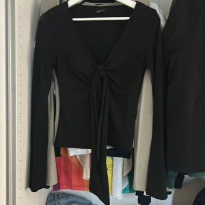 Svart långärmad topp med knyt - Snygg svart långärmad topp med djup v-ringning och knyt framtill. Perfekt att styla med jeans eller kjol för en trendig look. Toppens material är stretchigt och sitter snyggt på kroppen. Har använt ett antal gånger men den är ändå i ett bra skick. Pris kan diskuteras 