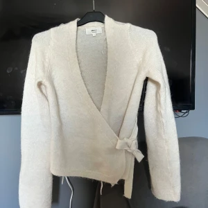 Beige omlottkofta från Gina Tricot - Mysig beige omlottkofta från Gina Tricot i ullblandning. Koftan har långa ärmar och knyts i sidan med ett band. Perfekt för lager-på-lager och en stilren look.