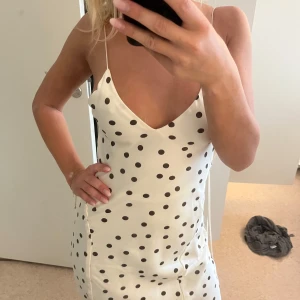 Vit lång prickig klänning från Zara - Supersnygg långklänning från Zara i vit satin med brunsvarta prickar. Klänningen har smala axelband, v-ringning och en elegant omlottkänsla baktill. 