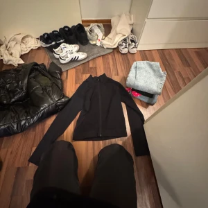 Svart träningsjacka från 157 - Svart träningsjacka från 157 med hel dragkedja framtill och lång ärm. Jackan är i ett stretchigt syntetmaterial som passar perfekt för aktiva dagar. Enkel och clean design utan mönster, perfekt för dig som gillar sportig stil.