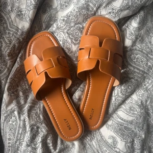 Bruna sandaler från Nelly  - Snygga bruna sandaler från Nelly med trendig flätad rem över foten. Platt sula och öppen tå gör dem perfekta för varma dagar. Stilren design som passar till många outfits. endast testade