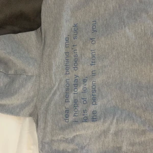 Grå hoodie med blått tryck - Snygg grå hoodie med blå text på ryggen: 'dear person behind me, i hope today doesn't suck. lots of love, the person in front of you'. Tröjan ska vara i storlek M men när jag beställde den var den super liten. Skulle säga att det är storlek XS istället! 🥹🥹