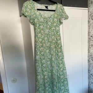 Grön blommig långklänning från Lindex - Superfin långklänning från Lindex i ljusgrönt med små vita och ljusblå blommor. Klänningen har v-ringning, korta ärmar och knytband i midjan för en snygg passform. Perfekt för sommarens alla tillfällen!
