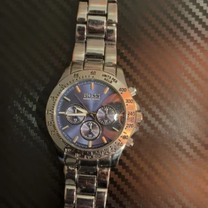 Klocka - Stilren med silverfärgat armband i metall och blå urtavla. Klockan har tre mindre urtavlor, tydliga markeringar och kronograf-funktion. Perfekt accessoar för dig som gillar klassisk och modern stil.