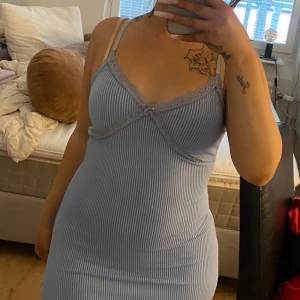 Ljusblå ribbad kortklänning med spets - Supersöt ljusblå ribbad kortklänning med smala axelband och spetsdetaljer vid urringningen. Klänningen har en liten rosett framtill och sitter tight för en snygg siluett. Perfekt för dig som gillar en feminin och enkel stil.