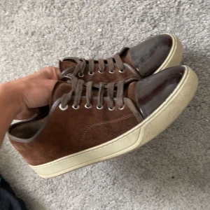 Bruna sneakers från Lanvin i mocka - Snygga bruna sneakers från Lanvin med ovandel i mocka och lackad tå. Skorna har vita gummisulor och klassisk snörning. Perfekta för dig som gillar stilrena och exklusiva sneakers med en twist.