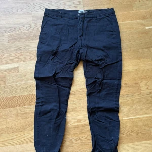 Svarta chinos - Svarta chinos från Lager 157. Byxorna har sidofickor fram och två bakfickor med knappdetalj. Upplevs större i storleken, passar även M.