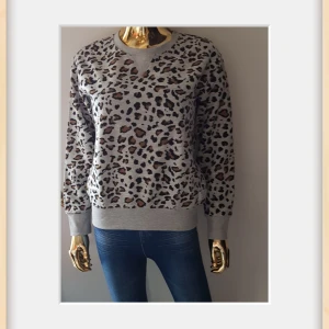NY Grå leopardmönstrad sweatshirt - Grå sweatshirt med leopardmönster i svart och brunt från State Athl. 1936. Tröjan har rund hals, ribbade muddar och lång ärm. Perfekt för dig som vill sticka ut med ett coolt djurmönster och ändå hålla det casual.Super Len och gosig insida 🥰