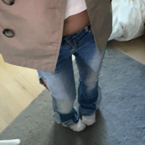Blå bootcut jeans med slitningar - Säljer ett par ljusblå bootcut jeans med slitningar och hål på låret. Jeansen har låg midja och är i klassisk denim med snygg tvätt och slitna detaljer. Perfekta för en avslappnad och trendig look.