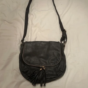 Svart axelväska med tofsar - Säljer en svart axelväska med justerbar rem och snygga tofsar 
