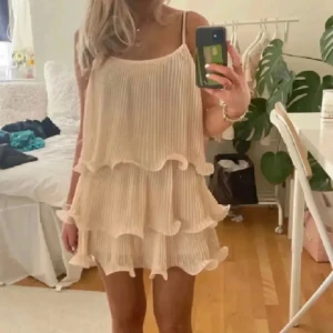 Champagnefärgad volangklänning H&M - Första och sista bilden är lånade. Superfin kort plisserad klänning från H&M i champagnefärg med tunna axelband och flera lager volanger. Lätt och flowy känsla, perfekt för sommarens varma dagar. Snyggt fall och riktigt söt modell som ger en romantisk vibe.