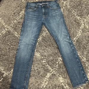 Emporio Armani blå jeans slim fit - Snygga blå jeans från Emporio Armani med klassisk femficksdesign och diskret logga på bakfickan. Jeansen har en slim passform och raka ben, tillverkade i mjukt denimtyg med lätt tvättad look. Perfekta för en stilren och modern vibe.