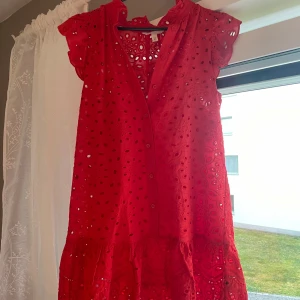 Röd kort klänning med broderade detaljer - Använd 1 gång och passar en S/M men är i xs!Superfin röd kort klänning från H&M med broderade hålmönster och volang nertill. Klänningen har v-ringning, knappar framtill och korta volangärmar. Perfekt för sommarens alla tillfällen och ger en riktigt söt vibe.