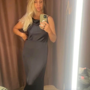 Svart långklänning från & Other Stories - Supersnygg svart/grå långklänning i satin från & Other Stories. Klänningen har tunna axelband, snörning i ryggen och en elegant slits.   Aldrig använd med prislapp kvar . Storlek 38