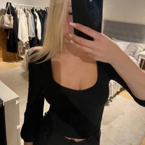 Svart topp med puffärm från ONLY - Svart topp från ONLY med fyrkantig ringning och lätt puffade axlar. Toppen har smickrande rynkdetalj framtill och är figurnära i modellen. Perfekt att styla med jeans eller kjol för en trendig look.