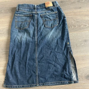 Lång jeanskjol ifrån Levis - Snygg lång jeanskjol från Levis 903 boot cut storlek M men passar bra på mig som har S så liten i storleken. Kjolen har två bakfickor, bälteshällor och en cool slits på sidan för extra edge. Perfekt för dig som gillar en avslappnad men trendig stil. Det är uppsytt lite på slitsen så den inte går lika långt, man kan se på sista bilderna, går att sprätta upp om man vill😊