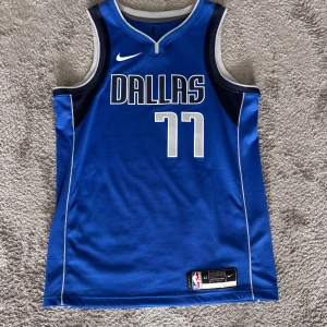 Dallas Mavericks Doncic baskettröja Nike - Blå Dallas Mavericks baskettröja med nummer 77 och Doncic på ryggen. Tillverkad i ventilerande Dri-FIT-material, ärmlös modell med vita och mörkblå detaljer samt vit Nike-logga på bröstet. Perfekt för dig som vill representera Luka Doncic på planen eller läktaren.