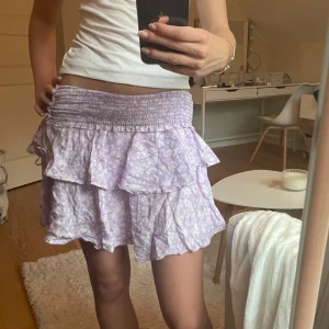 Ljuslila blommig volangkjol xs - Supersöt kort volangkjol från Samsa Collection i ljuslila med vitt blommönster. Kjolen har smockad midja och dubbla volanger som ger en flowy och lekfull vibe. Perfekt för varma dagar när du vill känna dig extra söt och somrig. Säljer då den inte kommer till användning 💓 köpt på Ullared