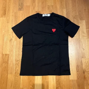 Svart Comme des Garçons Play t-shirt - Svart t-shirt från Comme des Garçons Play med klassisk röd hjärtlogga med ögon broderad på bröstet. T-shirten har rund halsringning och korta ärmar. Tillverkad i mjuk bomull och har en clean, stilren look som funkar till allt.