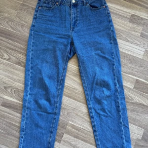 Blå jeans Betty från Lindex, strl 42 - Blå jeans från Lindex i modellen Betty. Hög midja och raka ben med normal passform. Jeansen har fem fickor, bälteshällor och stängs med knapp och dragkedja. Perfekta till sneakers eller boots.