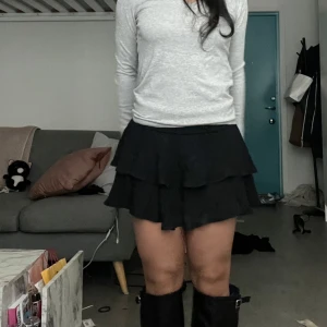 Svart volangkjol med lager på lager - Supersöt svart kortkjol med flera volanglager som ger en riktigt flowy och lekfull look. Kjolen har en lätt utsvängd form och sitter snyggt i midjan. Perfekt för dig som gillar en trendig och feminin stil.