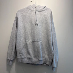 Grå hoodie från BikBok med huva - En basic ljusgrå hoodie från BikBok i storlek M. Tröjan har en stor känguruficka framtill, dragsko i huvan och ribbade muddar vid ärmslut och nederkant. Perfekt för chill dagar eller när du vill ha en enkel och clean look.