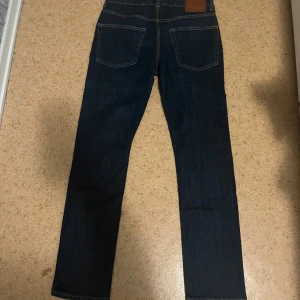 Mörkblå jeans från 157, straight fit - Snygga mörkblå jeans från 157 i rak modell. Klassisk femficksdesign med kontrastsömmar och läderpatch bak i midjan. Jeansen är tillverkade i bomull och har en normal passform som funkar till det mesta. Perfekt för dig som gillar stilrena och tidlösa jeans.