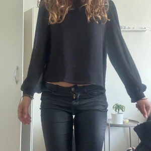 Svart blus  - Säljer en svart blus med långa, lätt transparenta ärmar och en snygg detalj med öppning i nacken. Blusen har en rak, lite lös passform och är tillverkad i ett tunt, matrial.