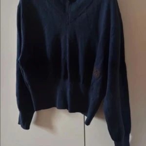 Mörkblå merinoulltröja från Totême - Snygg mörkblå stickad tröja från Totême i 100% merinoull. Modellen har v-ringning, croppad passform och långa ärmar. Totême-logga på bröstet ger en clean och stilren look. Perfekt till jeans eller kjol för en chill vibe.