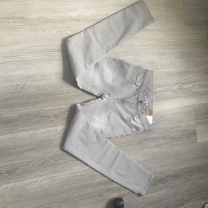 Grå slim jeans från D.M.D, strl 164 - Snygga grå jeans från D.M.D i modellen Alex, med regular waist och slim leg. Klassisk femficksdesign och bälteshällor. Perfekta för dig som gillar en stilren look med smal passform. Materialet är mjukt och bekvämt bomullstyg. De har aldrig varit andvända och prislappen är kvar