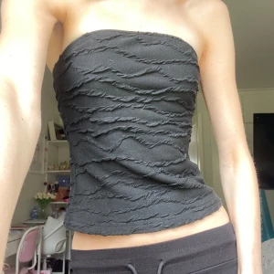 Svart tubtopp - Säljer en svart tubtopp med coolt strukturerat tyg och twistade vågiga detaljer över hela toppen. Modellen är bandeau och sitter tight över överkroppen. Perfekt att styla med jeans eller kjol för en trendig look❤️Så snygg till sommaren!! Står strl S, men sitter ganska tajt på mig vid brösten (jag har typ inga, väldigt små) och sitter löst vid midjan. Så vet ej storlek, XS och S🤷‍♀️💋