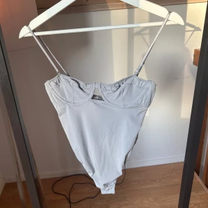 Ljusgrå korsettbody med smala band - Snygg ljusgrå korsettinspirerad body med tunna axelband och markerade kupor. Sitter tight och har en stilren, minimalistisk look. Perfekt att styla med jeans eller kjol för en trendig outfit. Aldrig använt