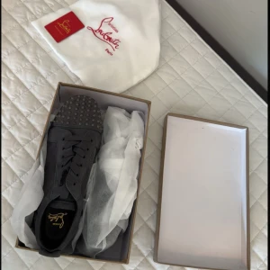 Christian Louboutin svarta sneakers med nitar - Helt nya och oanvända Svarta sneakers från Christian Louboutin i mocka med ikonisk röd sula och coola nitar på tån. Skorna har snörning och en stilren, rund tå. Perfekta för dig som vill sticka ut med en lyxig och edgy vibe. Vill ni ha fler bilder är det bara att fråga om det så skickar jag!