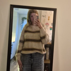 Randig stickad tröja från Sorbet - Supermysig stickad tröja från Sorbet i beige med breda bruna ränder och glittriga gulddetaljer. Tröjan har en loose fit, lång ärm och är perfekt för höst och vinter. Den är mjuk och fluffig, och passar dig som gillar en chill och trendig vibe. Har knappt blivit använda och har inga skador 