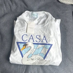 Vit Casablanca t-shirt med svanmotiv - Snygg vit t-shirt från Casablanca med stort tryck av en svan och blått grafiskt mönster på framsidan. T-shirten har klassisk passform, rund hals och korta ärmar. Perfekt för dig som gillar stilrena men ändå unika prints.