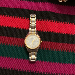 Citizen silver och guld armbandsur - Klassisk Citizen armbandsklocka i silver och guldton med länkarmband i metall. Urtavlan är vit med guldiga index och visare, samt dag- och datumvisning. Snygg och tidlös design som passar till många stilar.