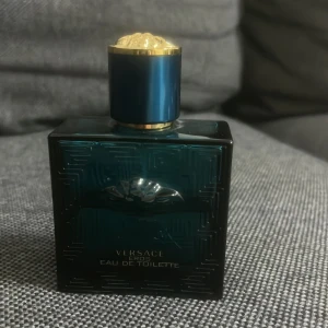 Versace Eros Eau de Toilette - Versace Eros Eau de Toilette i en lyxig, mörkblå glasflaska med guldiga detaljer och ett elegant mönster. Flaskan har en fyrkantig form och pryds av Versaces ikoniska Medusa-symbol. Perfekt för dig som gillar exklusiva dofter och snygg design. flaskan är 50 ml, och det är ungefär 35 ml kvar. (Tar inte emot returer) 