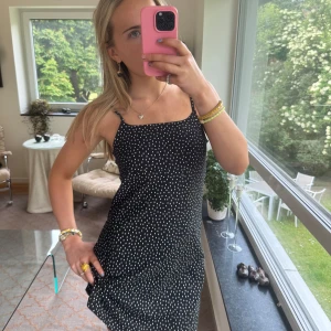 Svart prickig kort klänning - Supersöt svart kort klänning med vita prickar och tunna axelband. Den har en rak, enkel passform och är perfekt för varma dagar. Klänningen är ärmlös och har en lätt och luftig känsla, vilket gör den riktigt skön att bära.