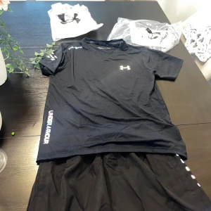 Svarta träningsshorts från Under Armour - Svarta träningsshorts från Under Armour i sportig modell med elastisk midja och snörning. Lätta och svala i syntetmaterial, perfekta för gymmet eller löprundan. Klassisk UA-logga och stilren look som funkar till alla träningspass.