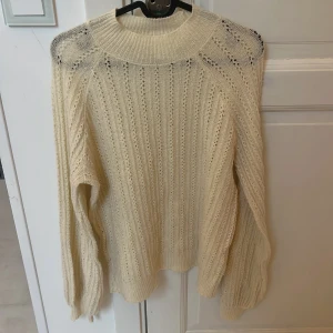 Beige stickad tröja från Vila - Supermysig beige stickad tröja från Vila med snyggt hålmönster och bred ribbad krage. Perfekt för lager-på-lager och passar till både jeans och kjol. Långärmad och lite loose fit för en chill vibe.