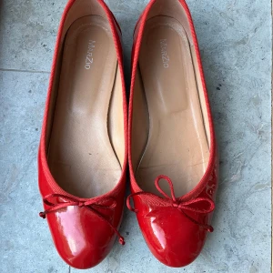 Röda ballerinaskor från Marzio - Snygga röda ballerinaskor i kalvskinn från Marzio i röd lack och söt rosettdetalj framtill. Skorna har rund tå och platt sula, perfekta för en färgstark look. Insidan är beige och de har en klassisk, enkel design.