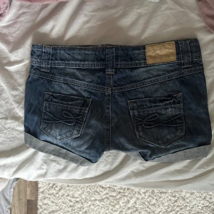 Lågmidjade jeansshorts  - Säljer ett par snygga mörkblå jeansshorts från Esprit med uppvikta benslut och coolt broderi på bakfickorna. Shortsen är i storlek W25 och passar XS till S Perfekta för sommaren och lätta att matcha med allt. Har en vit fäck på vänster ben men det är inget som man tänker på💗 hör av dig vid frågor💗💗
