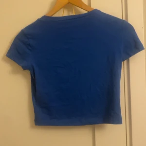 Blå croppad topp med kort ärm - Enkel och stilren blå croppad topp med korta ärmar. Perfekt att matcha med höga jeans eller kjol för en chill och trendig look. T-shirten har en klassisk rund halsringning och är gjord i mjukt material som känns skönt mot huden. Den är lite skrynklig men jag kommer stryka den och tvätta innan jag skickar iväg. 