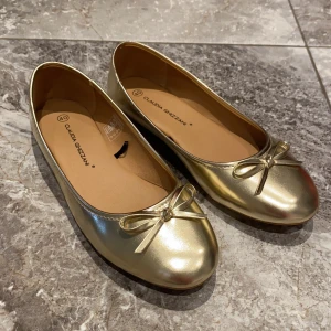 Guldiga ballerinaskor med rosett - Säljer ett par glansiga guldiga ballerinaskor från Claudia Ghizzani. Skorna har en söt liten rosett framtill och rund tå. De är helt nya. Jag har de i flera storlekar, inte bara 40. Säljer även likadana i svart och vit färg. Hör av er vid intresse💛