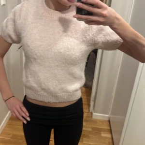 Ljusrosa stickad kortärmad tröja - Säljer en söt ljusrosa stickad tröja med korta ärmar och rund halsringning. Tröjan är croppad och har ribbade muddar vid ärmslut och nederkant. Perfekt för lager-på-lager eller som den är.