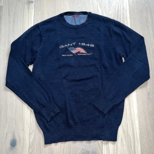 Mörkblå tröja från Gant med broderad flagga - Säljer en mörkblå tröja från Gant i storleken M. Tröjan är i 100% bomull och sitter väldigt avslappnat och skönt. Ny pris cirka 1000kr mitt pris 175kr. Säljer lite billigare då det är ett litet håll vid ”G” på framsidan av tröjan men det kan fixas enkelt. Hör av er vid några funderingar.