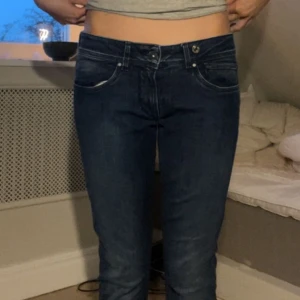 Mörkblå jeans med bootcut - Säljer ett par mörkblå jeans med klassisk femficksdesign och bootcut-ben. Jeansen har låg midja och kontrastsömmar, samt detaljerade bakfickor. Perfekta för en avslappnad stil.
